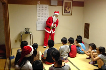 東京セントラルユースホステル施設内の和室で職員がサンタクロースに扮し子ども達とお話ししている姿