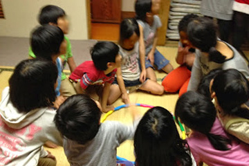 東京セントラルユースホステル施設内の和室で大人数の子ども達の中と職員が集まって仲良くお話ししている姿