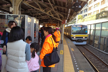 お母さんと子どもと東京セントラルユースホステルの職員がJR飯田橋駅で中央線の電車が来るのを待っている様子